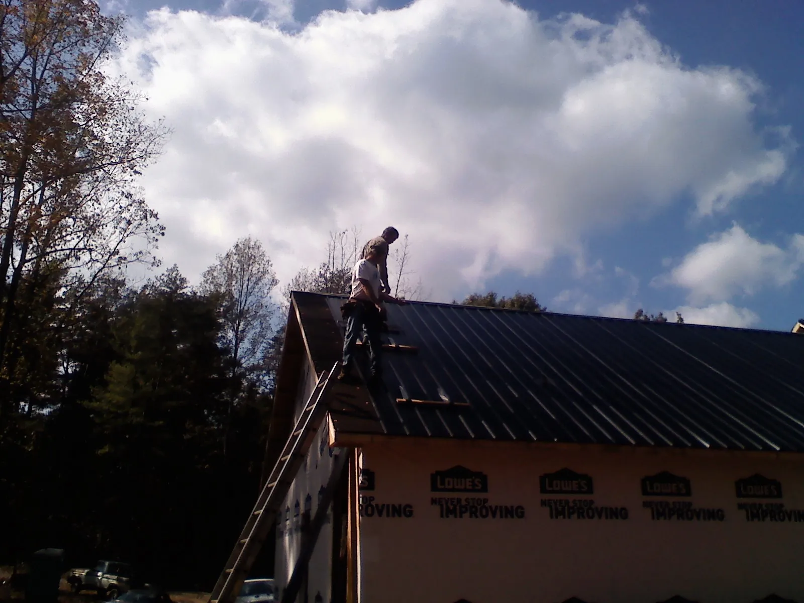 Roofer fastening dark metal panels high against a cloudy sky, from a Roof Inspection job in Holland