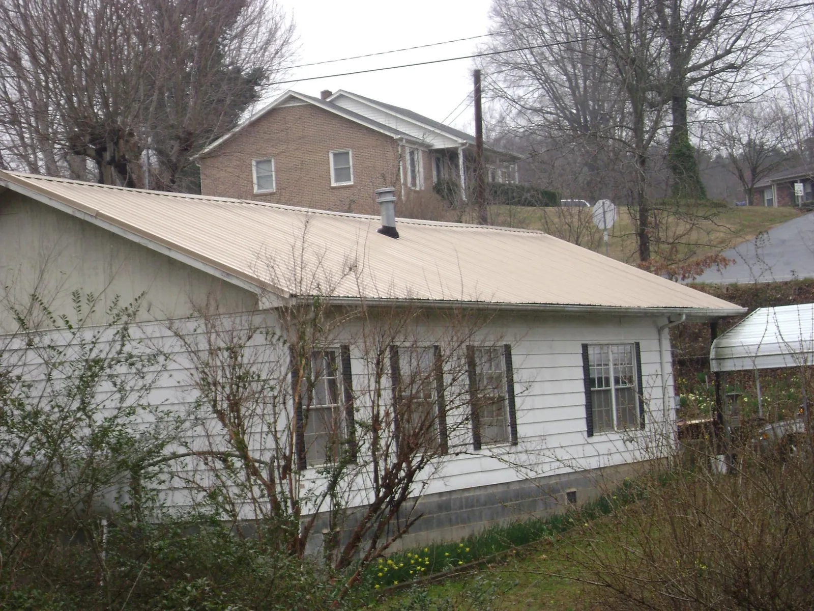 Tan metal roof on a white sided house set into a hillside — Commercial Roofing by Roofing Brothers in Holland