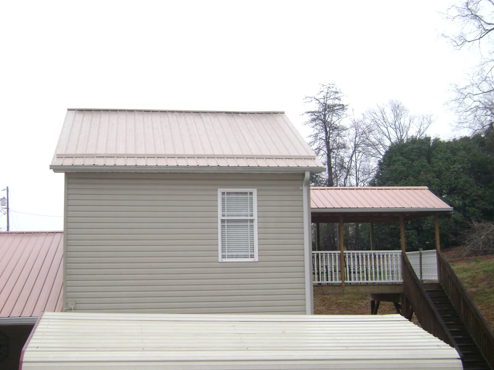 Tan metal roofs on a two story addition and attached porch, from a Roof Replacement job in Holland